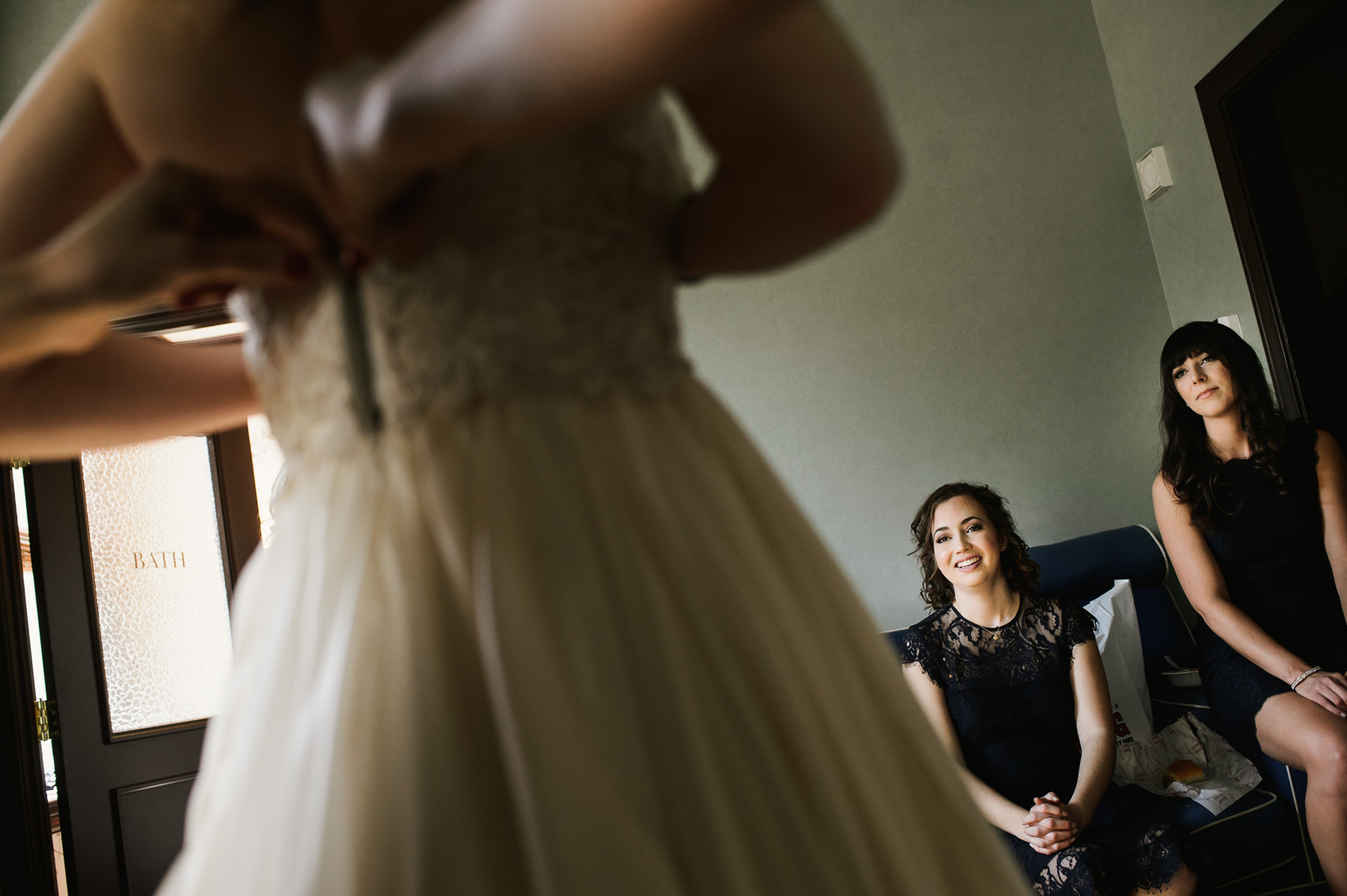 bridesmaids watching bride get in wedding dress