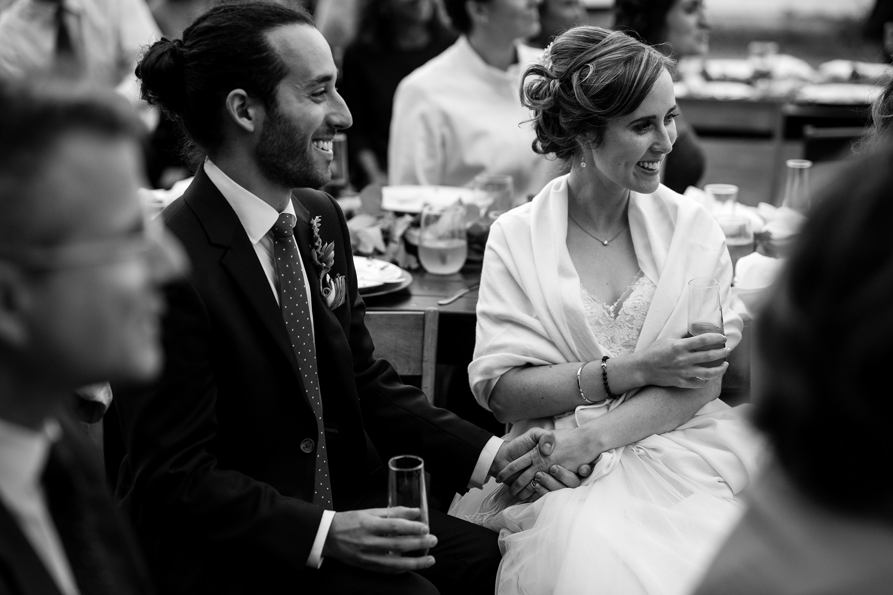 bride and groom hold hands while listening to wedding toasts
